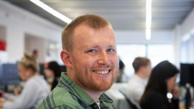 Headshot of Jake Ramsden. A man smiling, wearing a green shirt.