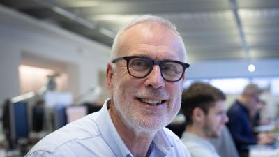 Headshot of Nicholas Rank. A smiling man wearing glasses and a blue shirt.