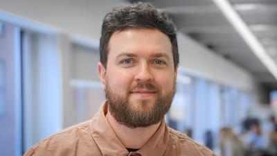 Headshot of Paul Wright. A man smiling, wearing a brown shirt.