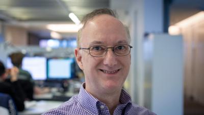 Headshot of Stephen Welsh. A man smiling, wearing glasses and a purple shirt.