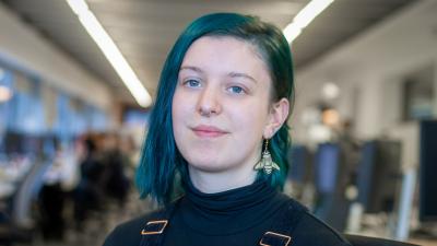 Headshot of Daisy Winter. A woman smiling with green/blue hair.