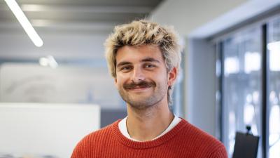 Headshot of Ed Kamal, a man wearing a red jumper smiling at the camera.
