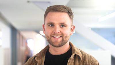 Headshot of Danny Atkinson, a man wearing a black t-shirt and brown jacket.