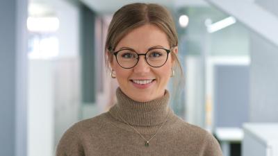 Headshot of Jenny, a woman smiling at the camera, wearing a brown turtleneck jumper.