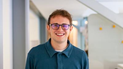 A man in a blue shirt and glasses standing in an office corridor
