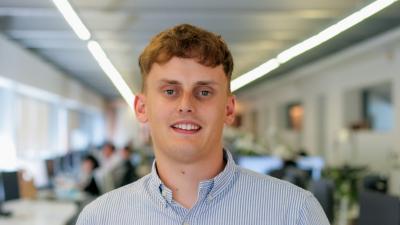 Headshot of a man wearing a blue shirt standing in the middle of an office.