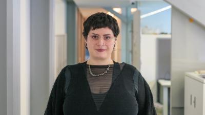 A person with dark hair and wearing a dark dress looking at the camera