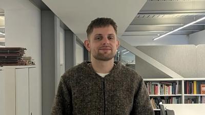 A man in a brown jumper standing in an office corridor