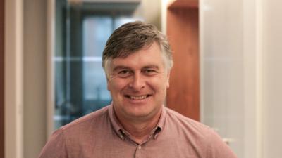 Man in a light red shirt standing in an office corridor