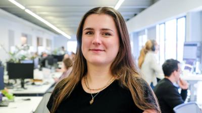 Headshot of a woman with brown hair and a black top standing in an open office.