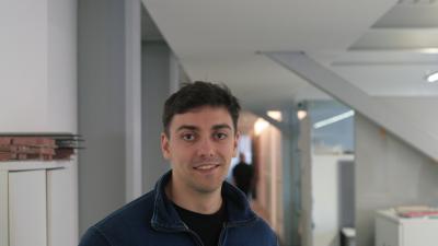 Photo of a man with brown hair and a blue jacket standing in a corridor.