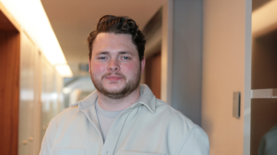 Man with brown hair and beard, wearing a light coloured shirt.
