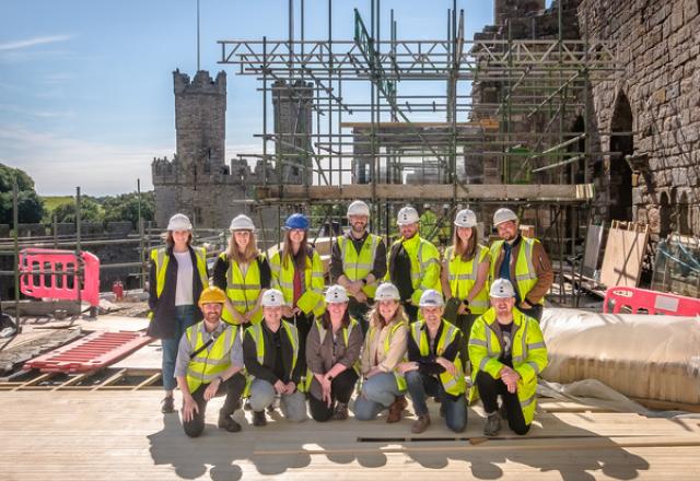 buttress staff posing in front of scaffolded castle