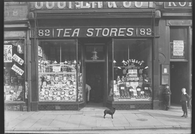 Black and white photograph of a street view of the front of a shop - the shop is called Tea Stores