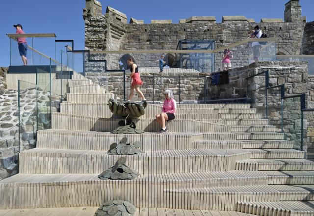 People sitting on the tiered timber seating, on the upper deck of Caernarfon Castle
