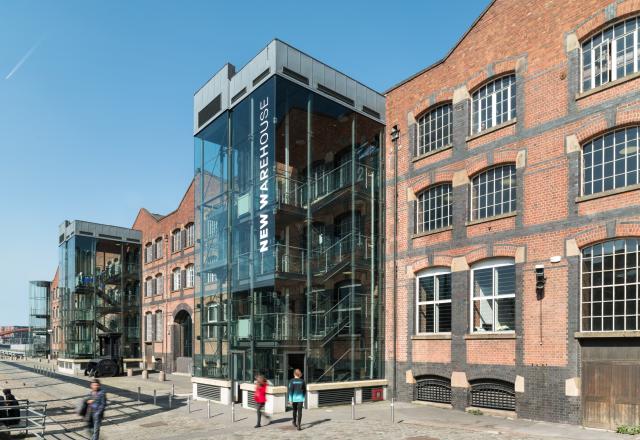External photograph of a very large Victorian warehouse with a modern glass tower.