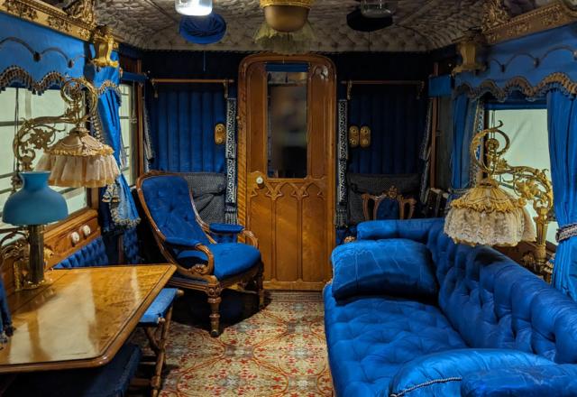Internal photograph of Queen Victoria's lounge carriage. The furnishings have a rich blue colour and this is in the decor. The ceiling is quilted. 