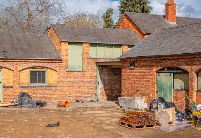 Delapre Abbey Stables pre-construction. Orange brick one-storey building with green doors.