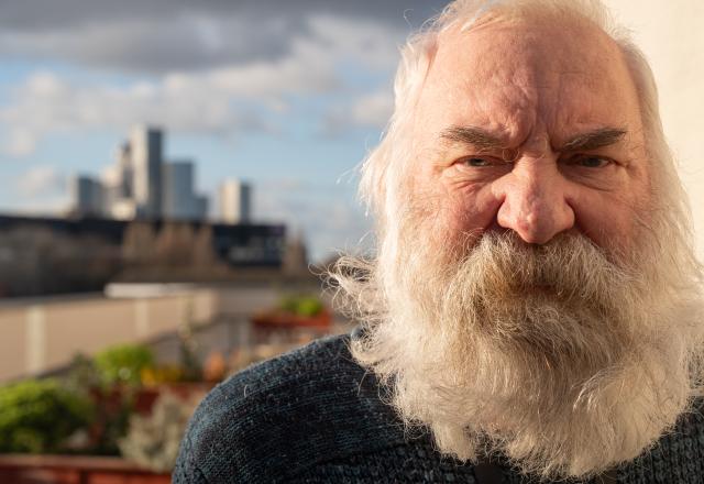 a portrait of man with large white beard with a city skyline as his backdrop