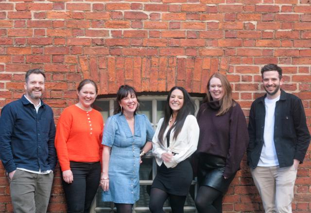 Six people standing in front a red brick wall outside.