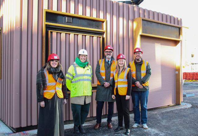 Five people wearing high vis vests and hard hats standing in front of a kiosk.