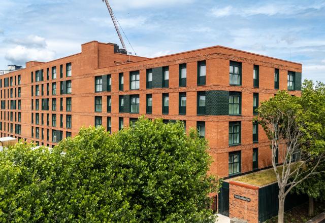 An aerial shot of a red brick apartment block building, surrounded by greenery.