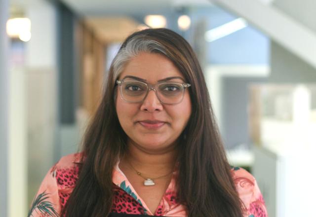 Woman with black long hair, wearing glasses and a pink shirt.