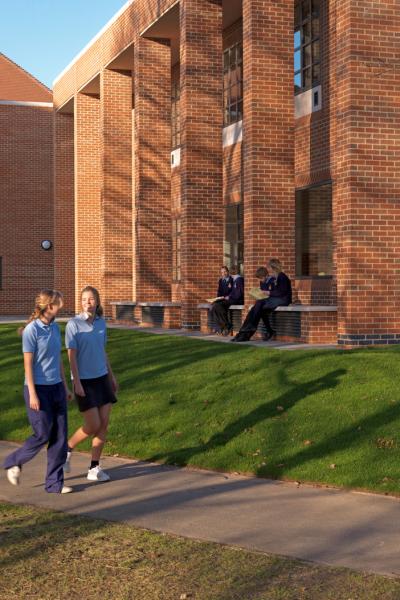 two schoolgirls in sports kit walk past a brick building