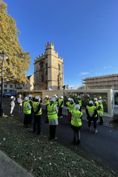 a group of people in hi vis stand in front of a stone building with scaffold up