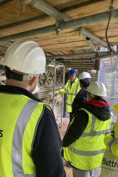 a group in hi vis and hard hats are being shown conservation work on the west front scaffold at lincoln cathedral