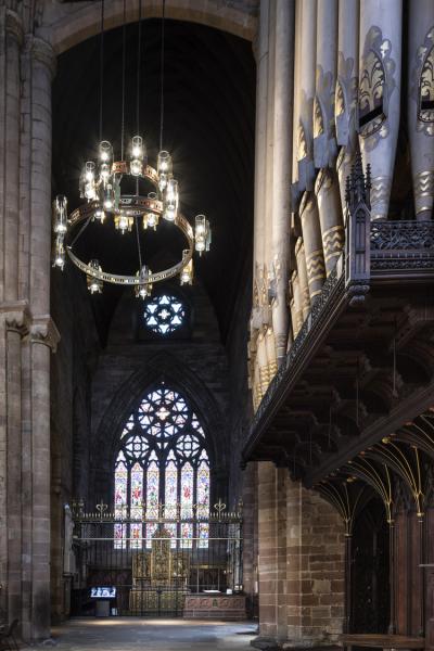 a stained glass window is seen in the dark interior of Carlisle cathedral