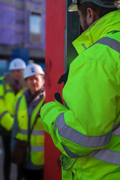 a man in a high vis coat is in the foreground describing details to a group on a building site