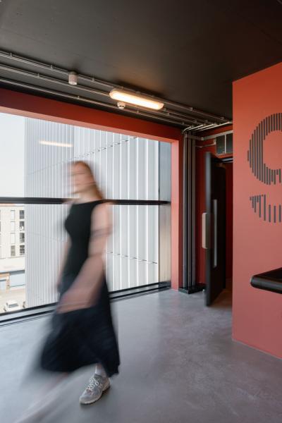 Modern stairwell with red walls, large window, and a '9' floor marker; a person walks through the space.