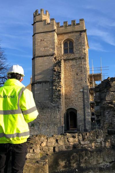 a man is stood with his back to the camera in a high vis jacket he ls looking at a ruined castle