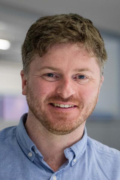 Grant Prescott - man in a blue shirt and dark blond hair, smiling.
