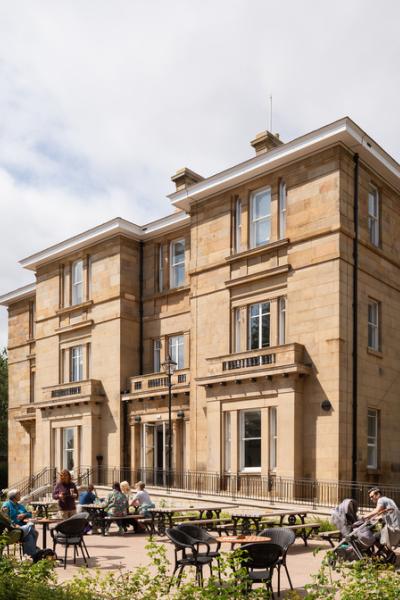 Exterior of an historic mansion house set within garden grounds and an open picnic area