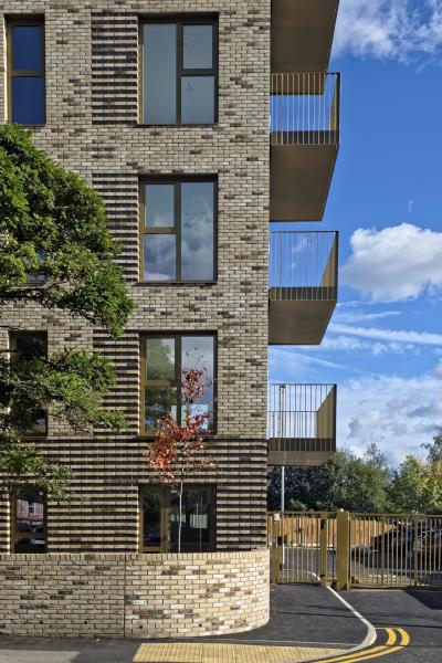 A side building shot of light brick apartments with balconies to the right-hand side, with a blue sky behind.