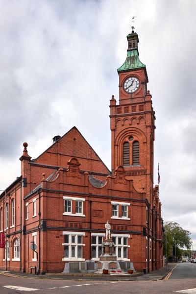 A heritage red brick building with a clock tower with a green pitched roof.
