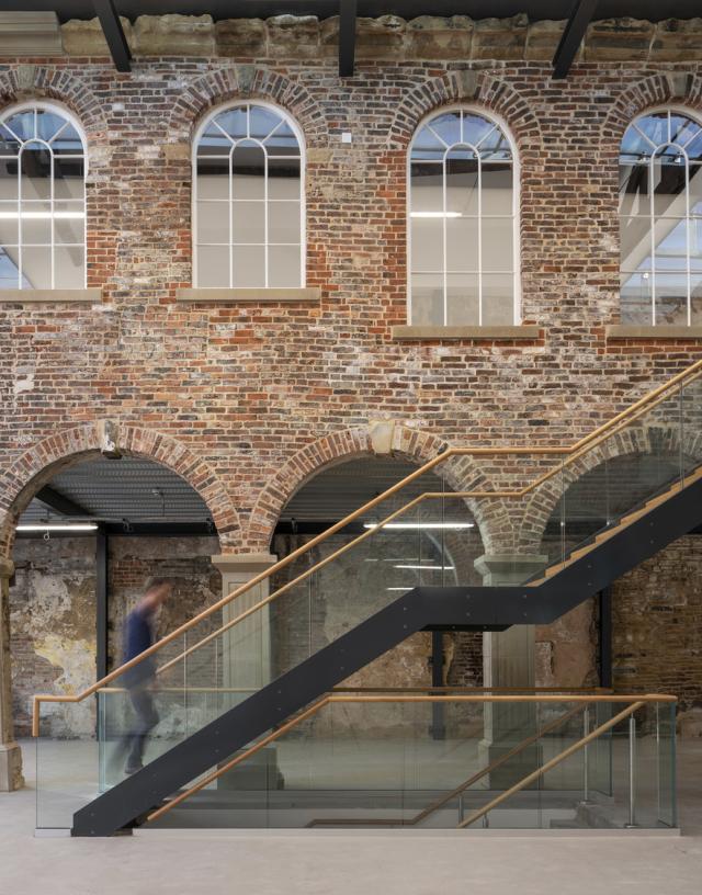 a man walks up a glazed staircase in front of a brick wall with arched windows