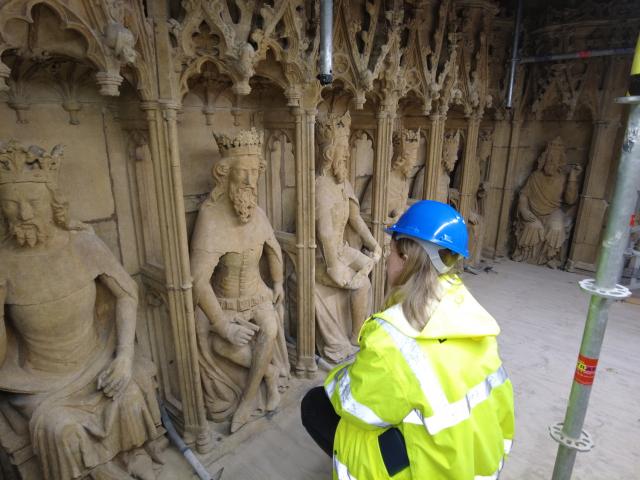 person in hi-vis crouching down to look at heritage stonework