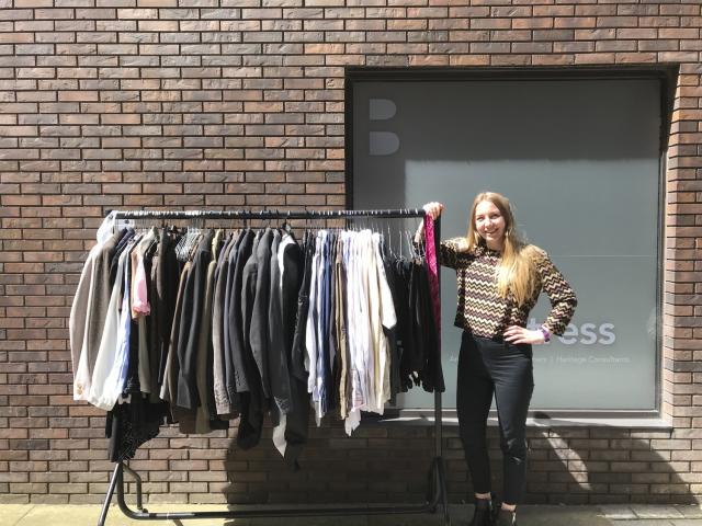 grace avery outside of the studio, standing next to clothes rail of donated clothes