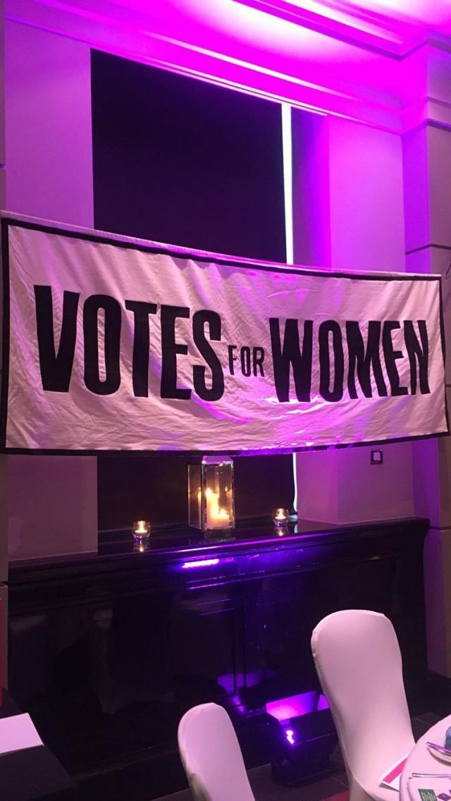 banner across room that reads 'votes for women' under pink lighting