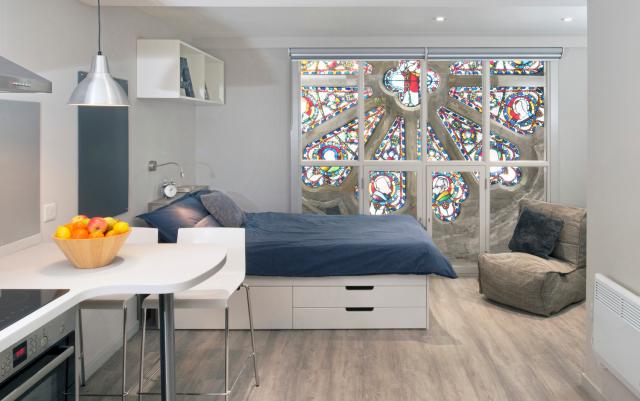 A bedroom inside a restored chapel with a stained-glass window.