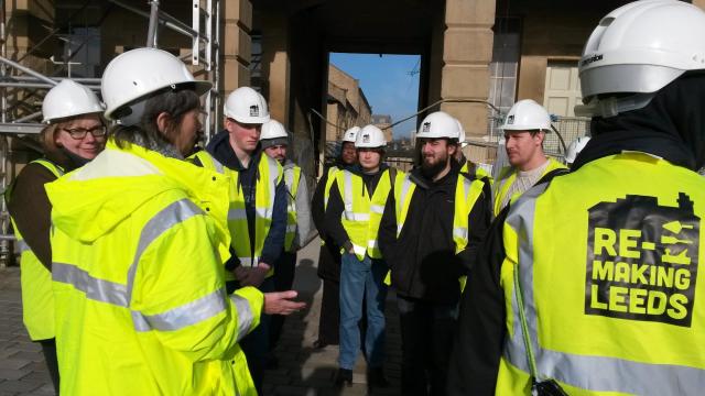 group of people in hi-vis and hard hats gathered at building site
