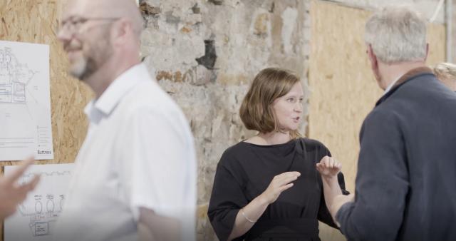 a lady in a black jumpsuit is talking at a consultation event