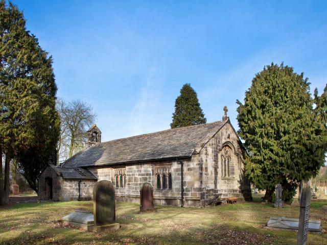 exterior of small church and cemetery in sunlight with greenery and trees