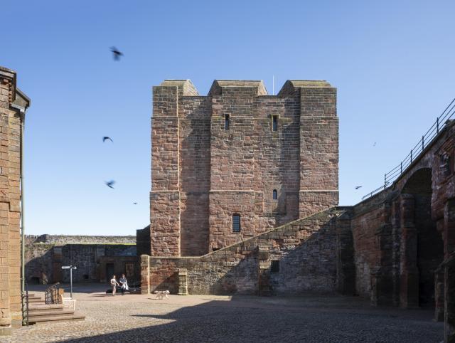 birds fly past the sandstone keep at Carlisle Castle on a sunny day