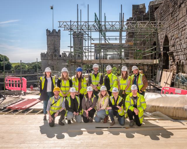 A group photo of some of the Buttress team in high-vis jackets, at Caernarfon castle in front of scaffolding.