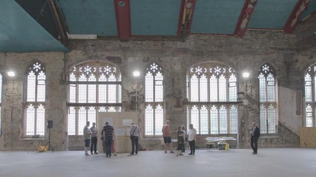 internal photograph of a Victorian, church-like hall with gothic arched windows. The hall is empty apart from three or four people viewing an exhibition board, Photograph taken at the public consultation for the plans.  