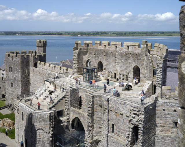 External photograph of a castle. It's taken from a drone so you see the internal high platform of the King's Gate. It has a wooden floor with people milling around enjoying the view and the sunshine. 